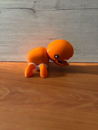 Figurita de juguete naranja con una expresión amigable, en posición de arrodillado.